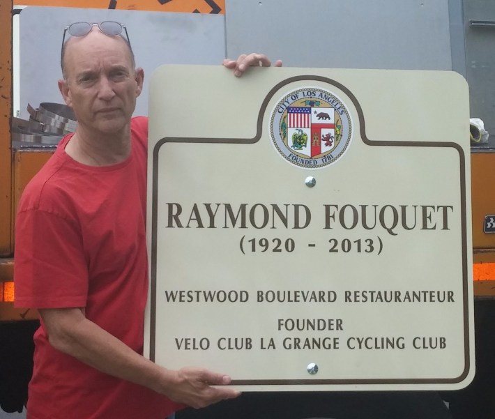 Former La Grange and City Bicycle Advisory Committee head Jay Slater with city signage for Raymond Fouquet Square commemoration. Photo via La Grange