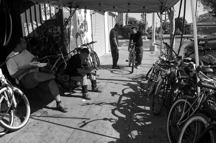 Santiago Galvez (hat), owner of Jesus' Bike Shop consults with a customer while youth who hang out at the shop and sometimes help out look on. Sahra Sulaiman/Streetsblog L.A.
