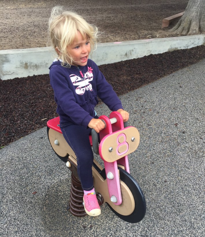 Maeve riding the playground bike