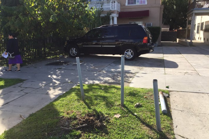 The front yard of this fourplex is already half-paved for parking. Posts (one of which lies prone) keep cars off the parkway.