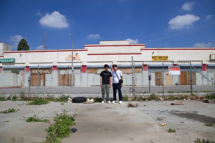 Juan Carlos Mercado and Miguel Sanchez stand in a vacant lot at Manchester and Vermont. The former swap meet site saw a groundbreaking two years ago but the mall project, planned by developer Eli Sasson, has yet to materialize. Sahra Sulaiman/Streetsblog L.A.