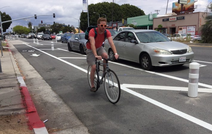 Cyclist riding past BikeRoWave on Venice Boulevard's new parking protected bike lanes