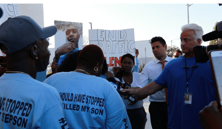 As the meeting at the constituent center came to a close, Woon's mother, Beverly Owens, and friends and supporters showed up with press in tow to demand justice. Owen's shirt reads, "You Should Have Stopped. You Killed My Son."