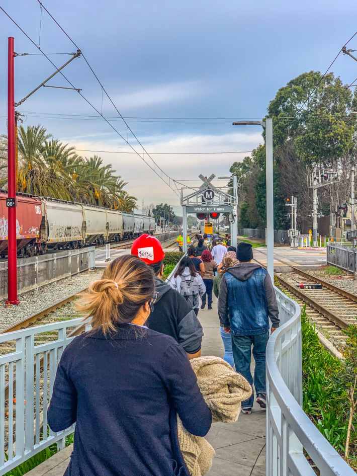 Blue Line riders, after exiting at the 103rd/Watts Towers station, wait to cross the tracks in order to access Metro’s bus shuttles to continue their trip south. Photo by Brian Addison.