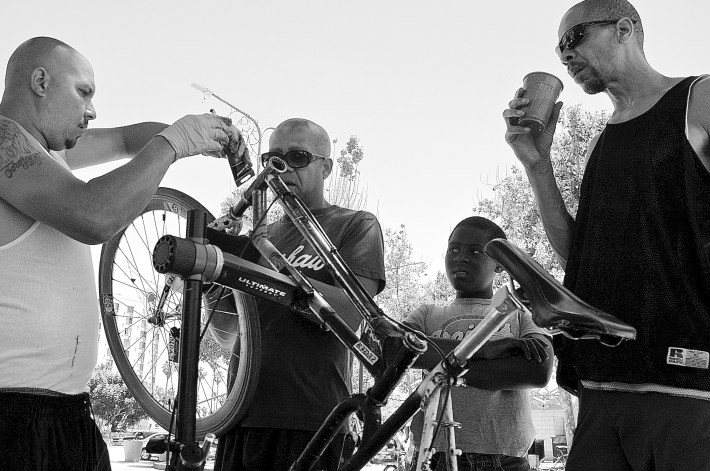 Cortez Wright watches BKoB members Mike Glasco (second from left) and Tony Kee (at right) help someone fix their bike at a tune-up session. Sahra Sulaiman/Streetsblog L.A.