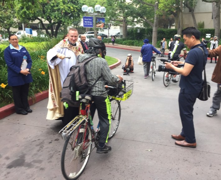 Reverend Bell splashes holy water to bless cyclists