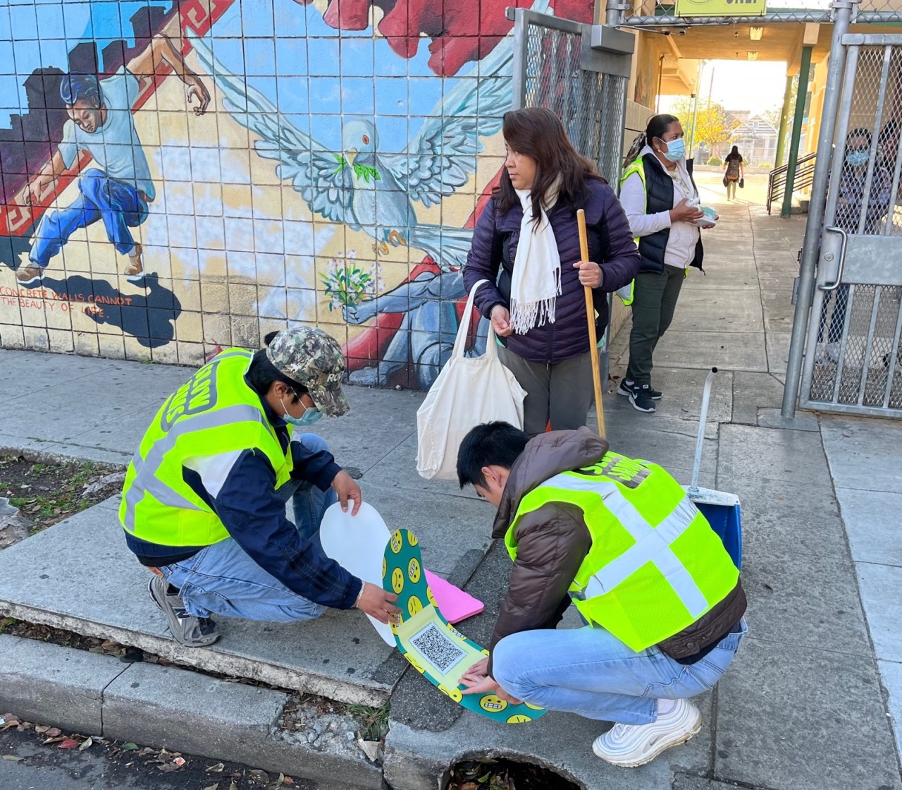 University Park Slow Jams volunteers applying a large band-aid to a lifted sidewalk just outside the entrance to Norwood Street Elementary School